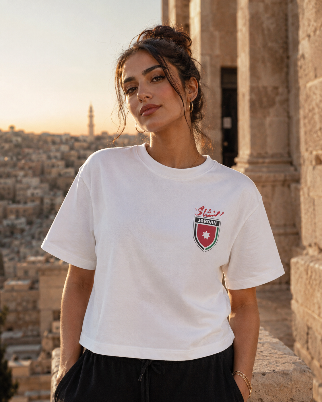 Woman wearing a white t-shirt with a logo, standing in front of stone architecture.